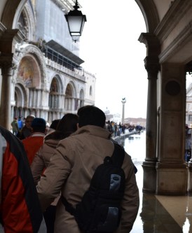 Pedestrians in single file, walking on "risers" above the flooded walkways.